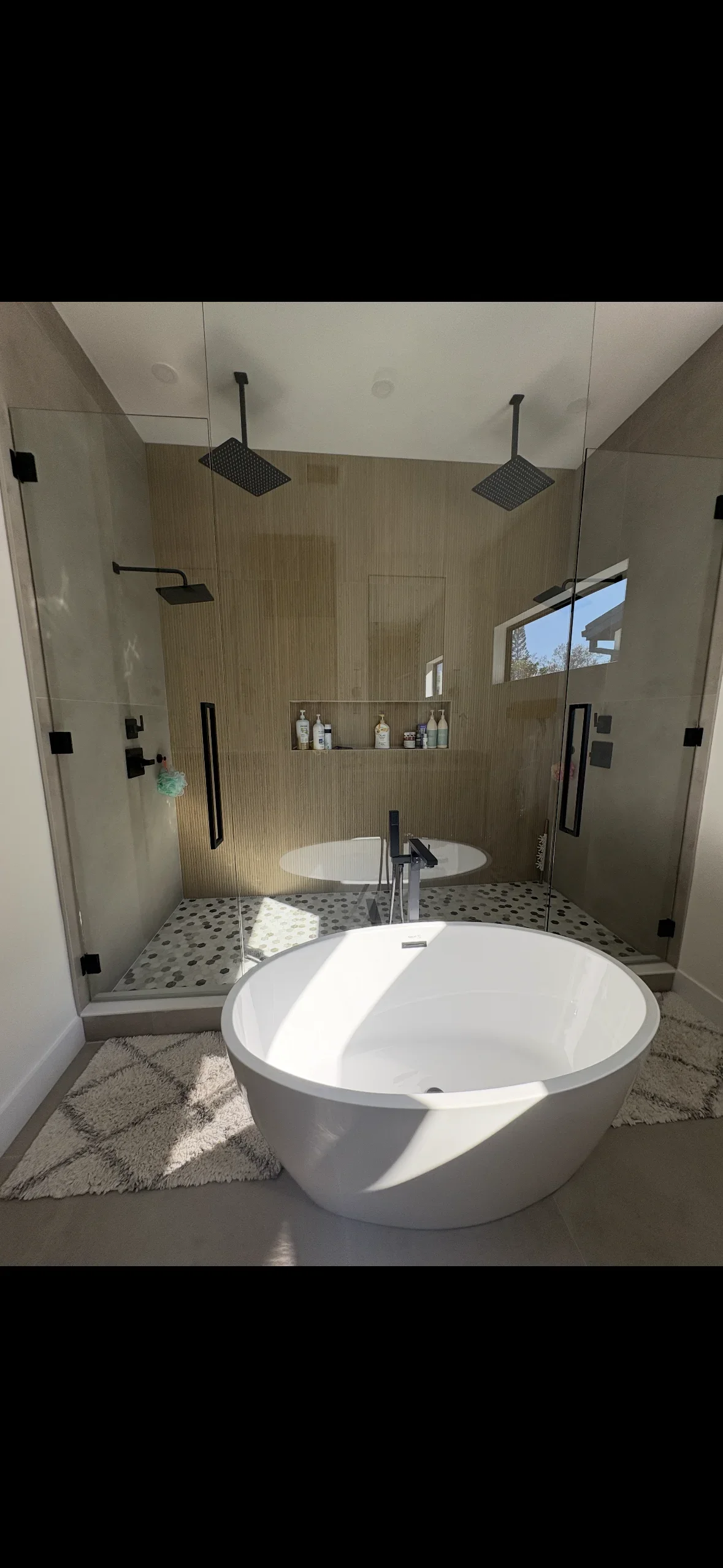 Luxury bathroom with wood-grain tile shower, pebble floor, frameless glass enclosure, and white soaking tub
