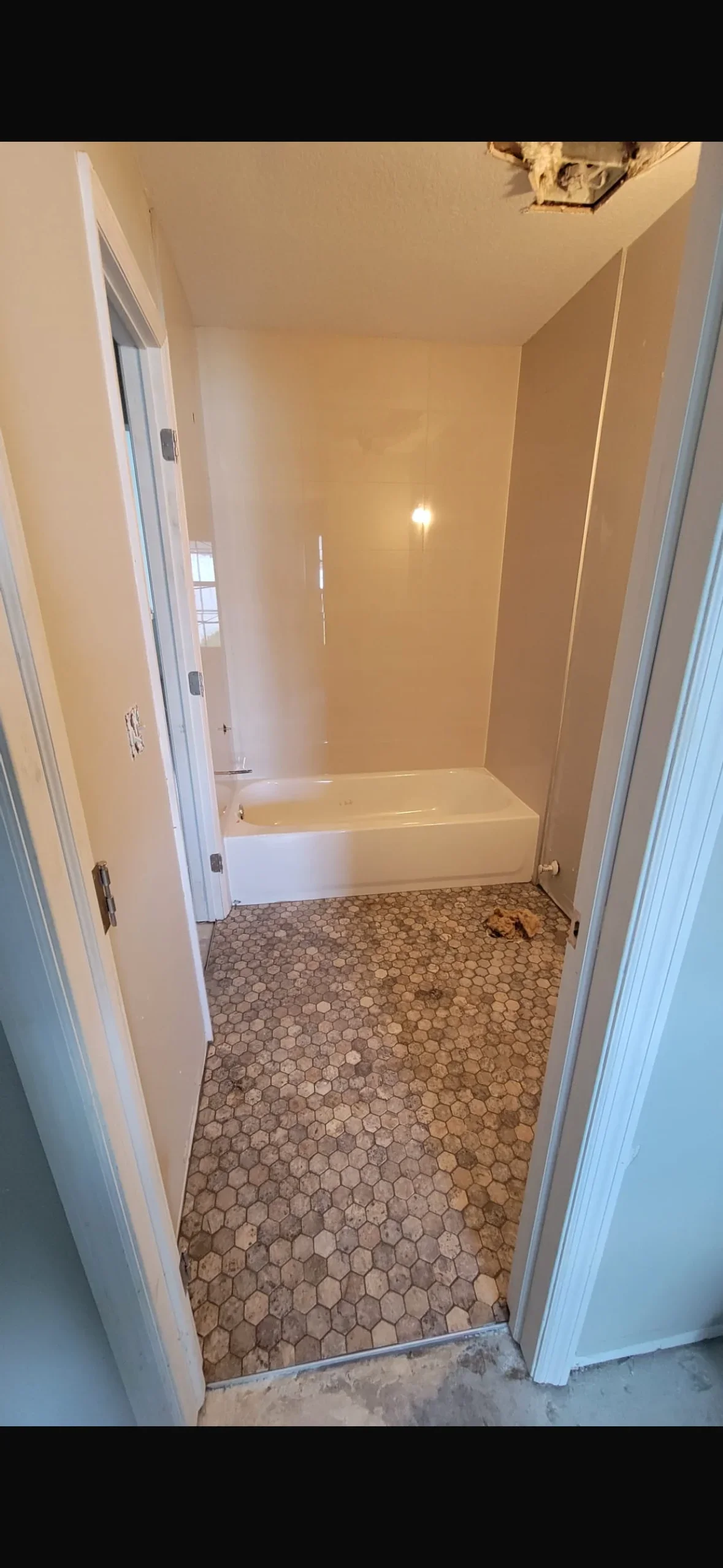 Hexagonal mosaic tile floor with white bathtub and finished drywall bathroom interior