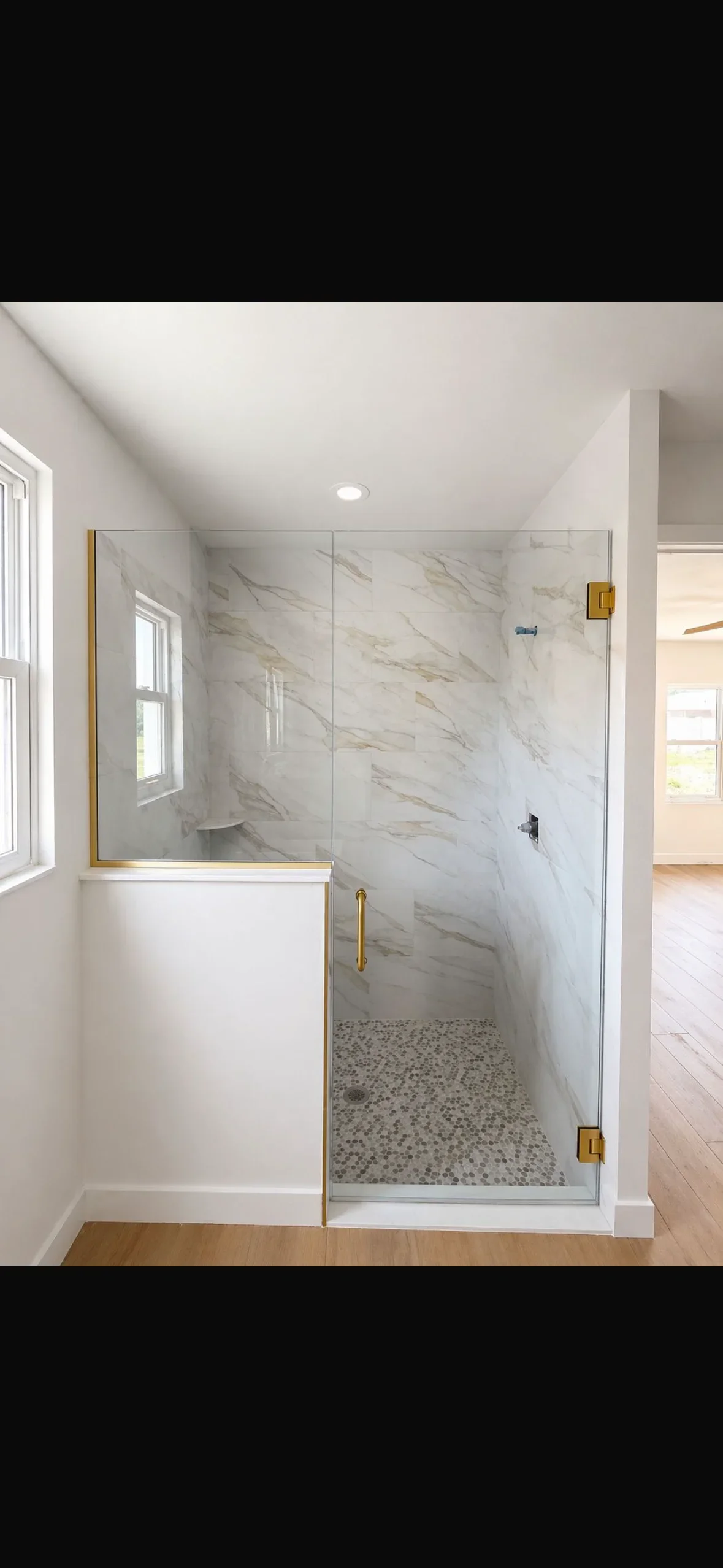 Marble tile shower with frameless glass doors, pebble floor, and brushed gold fixtures