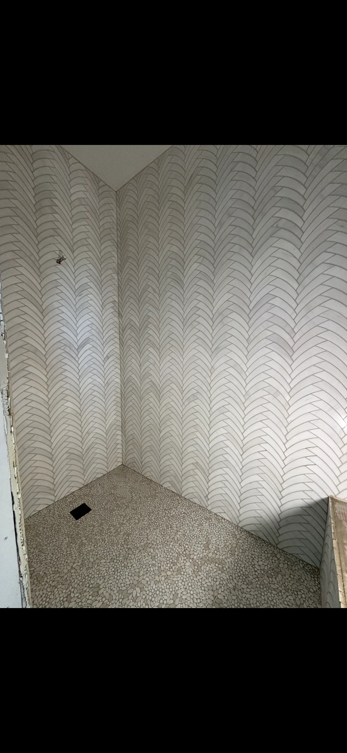 Herringbone pattern tile walls with pebble stone floor in shower installation
