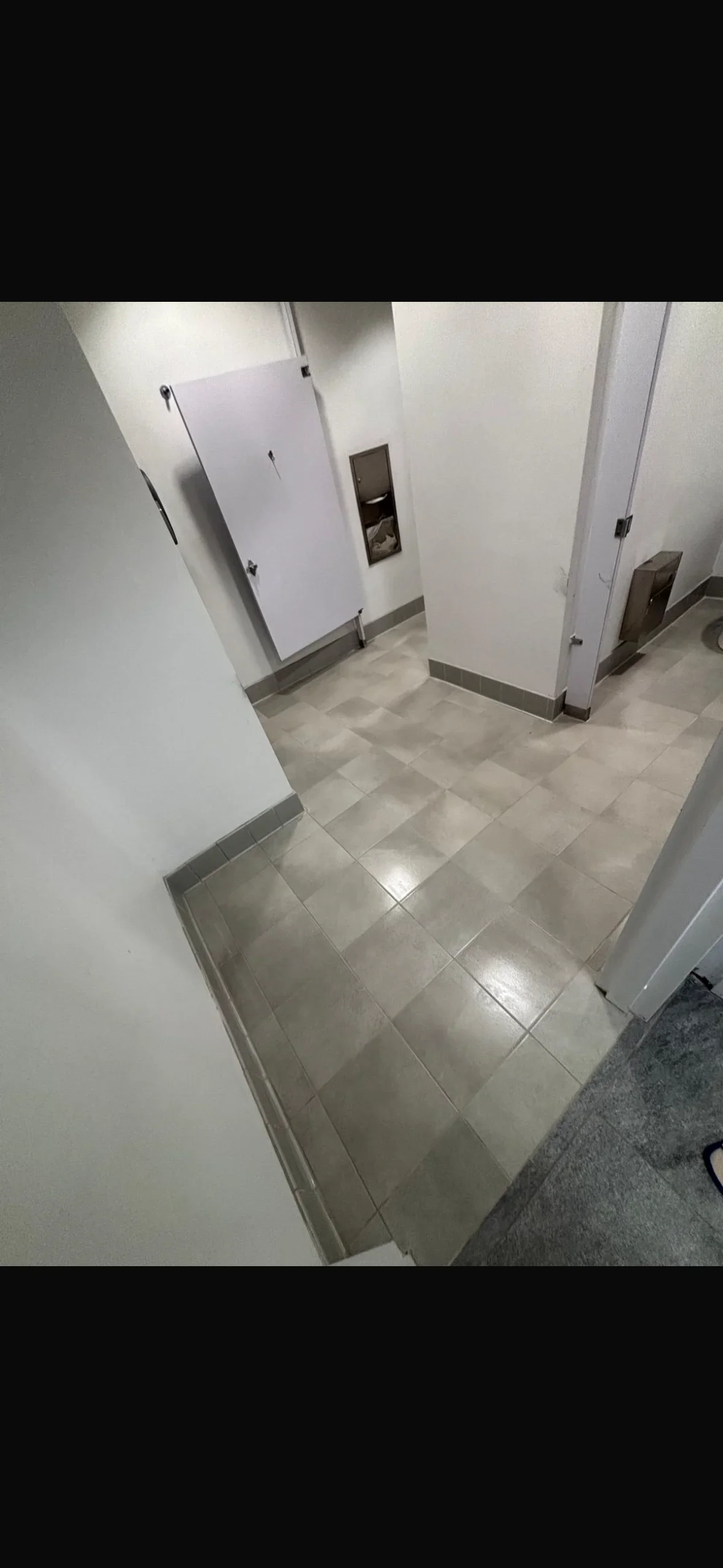 Commercial restroom with neutral ceramic tile flooring, white partition walls, and integrated fixtures