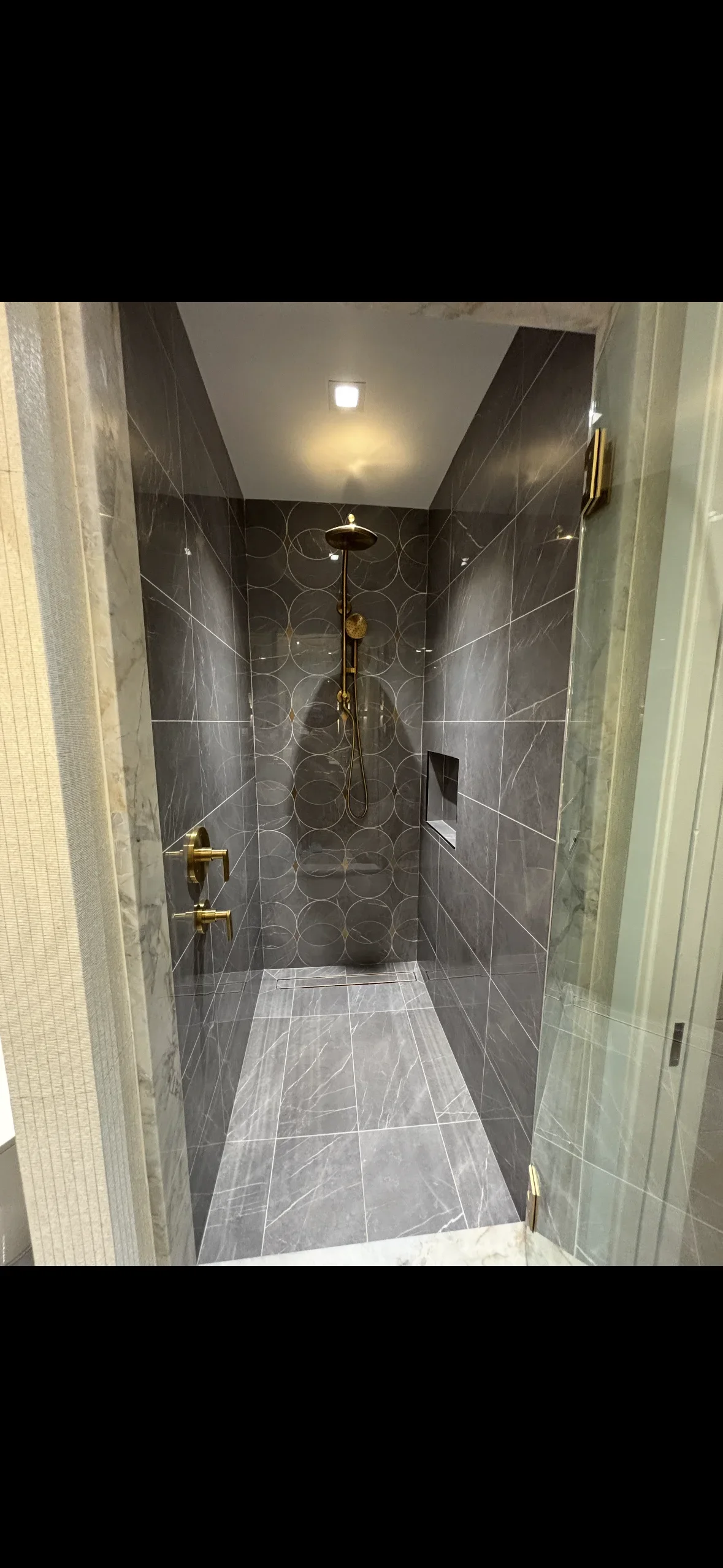 Dark marble tile shower with brass fixtures, frameless glass door, and polished floor