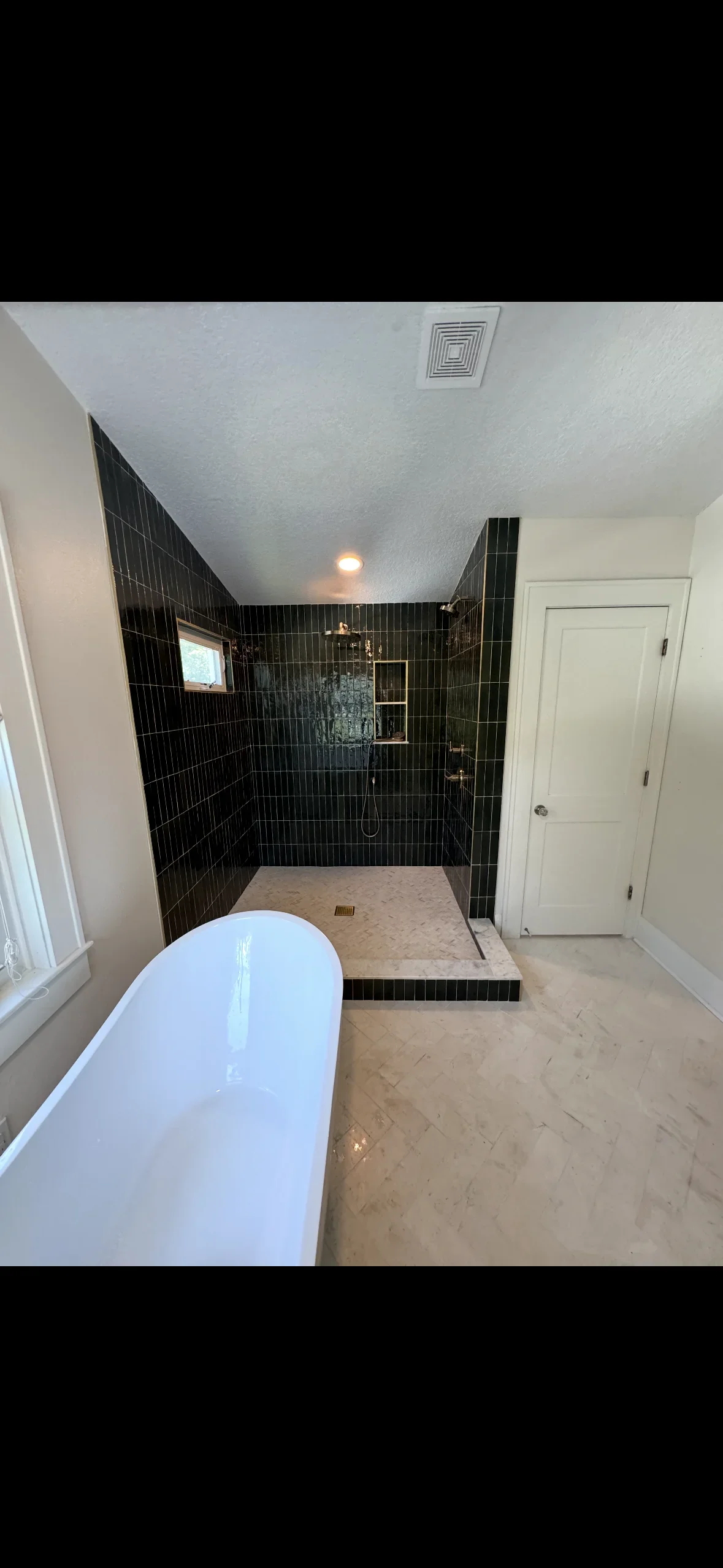Black subway tile shower with marble floor, glass enclosure, and white soaking tub in renovated bathroom