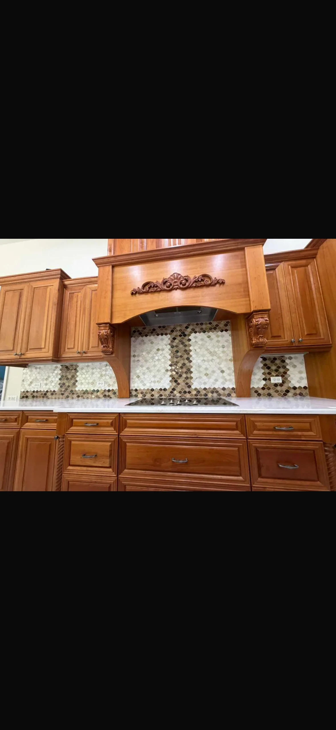Cream and dark stone mosaic tile backsplash installed behind kitchen counter with wooden cabinetry