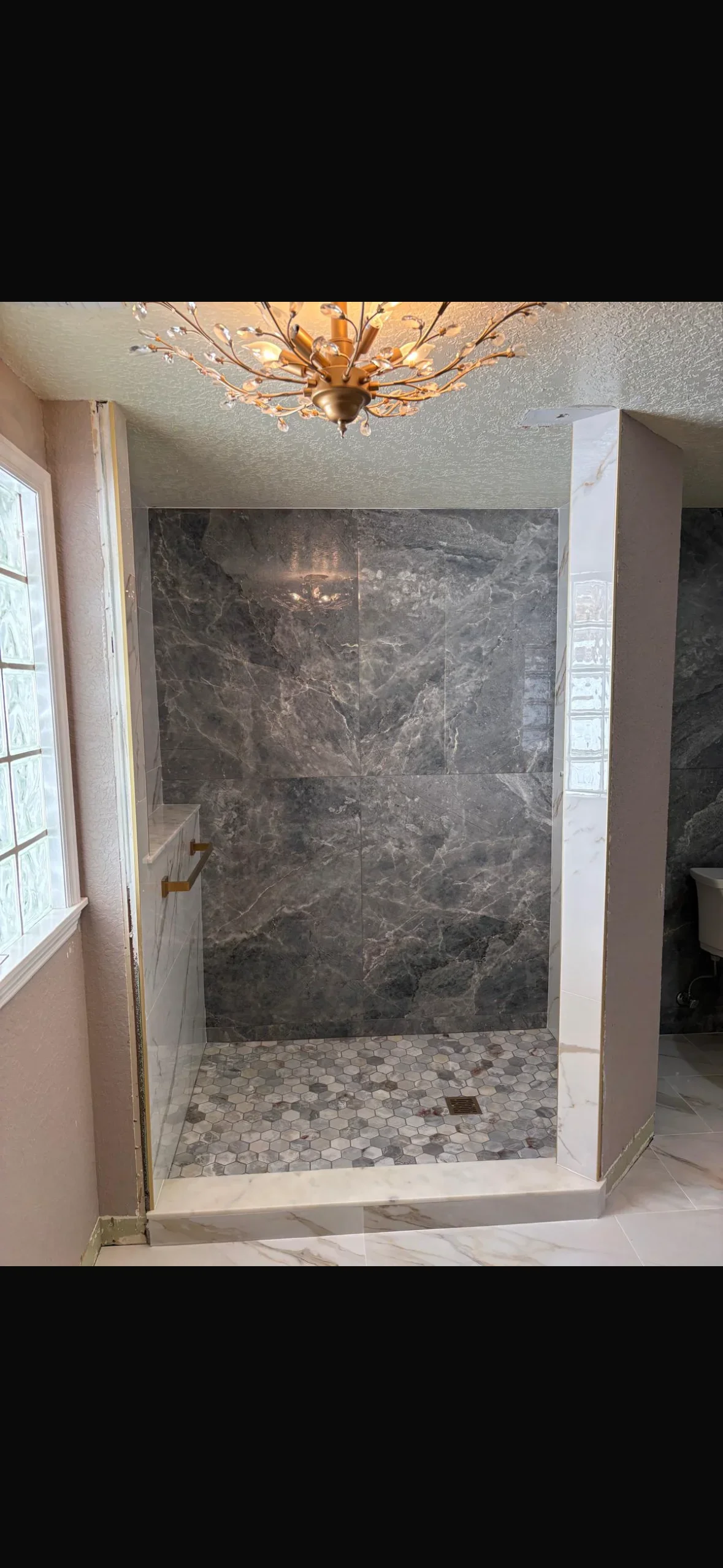 Dark marble tile shower walls with hexagonal mosaic floor and frameless glass enclosure
