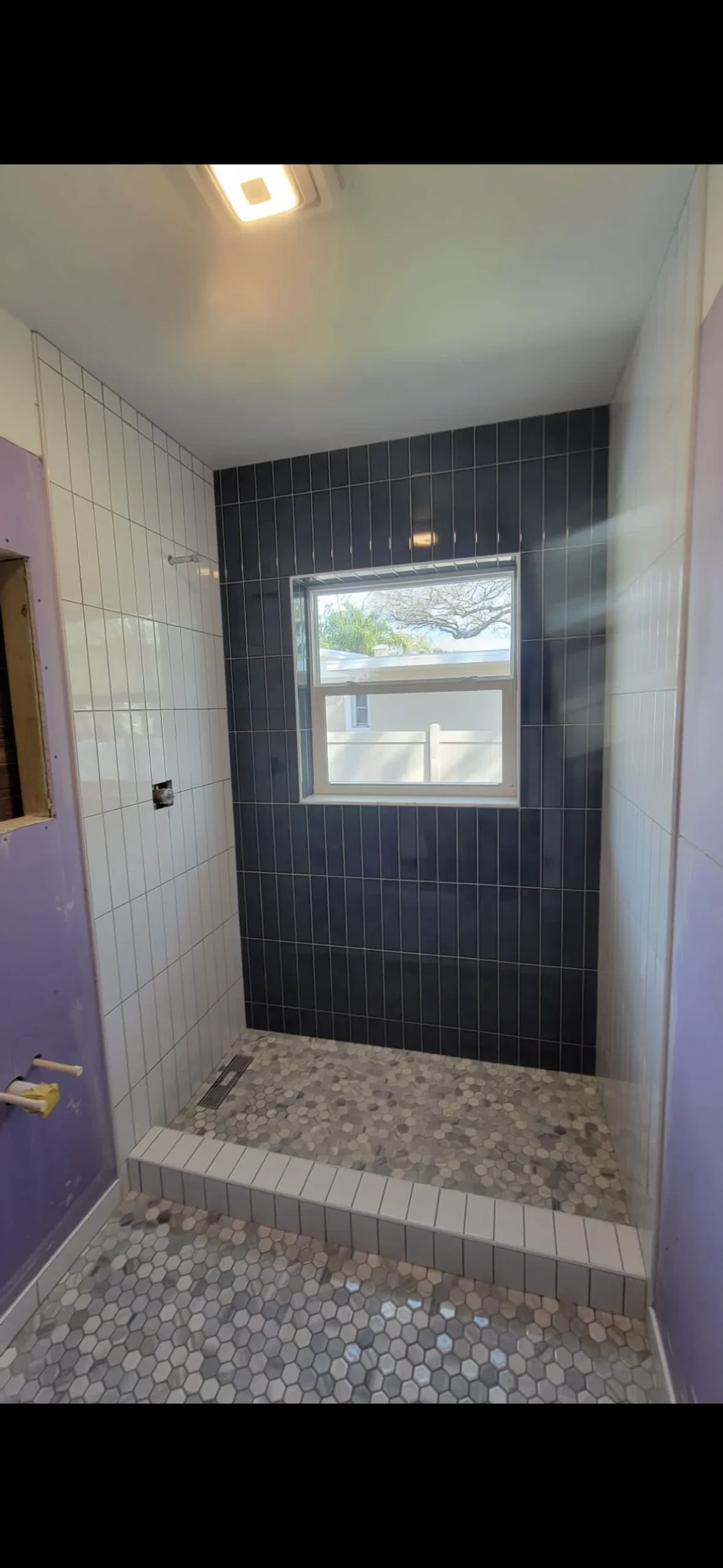 Shower with dark and white subway tiles, hexagonal floor mosaic, and recessed window
