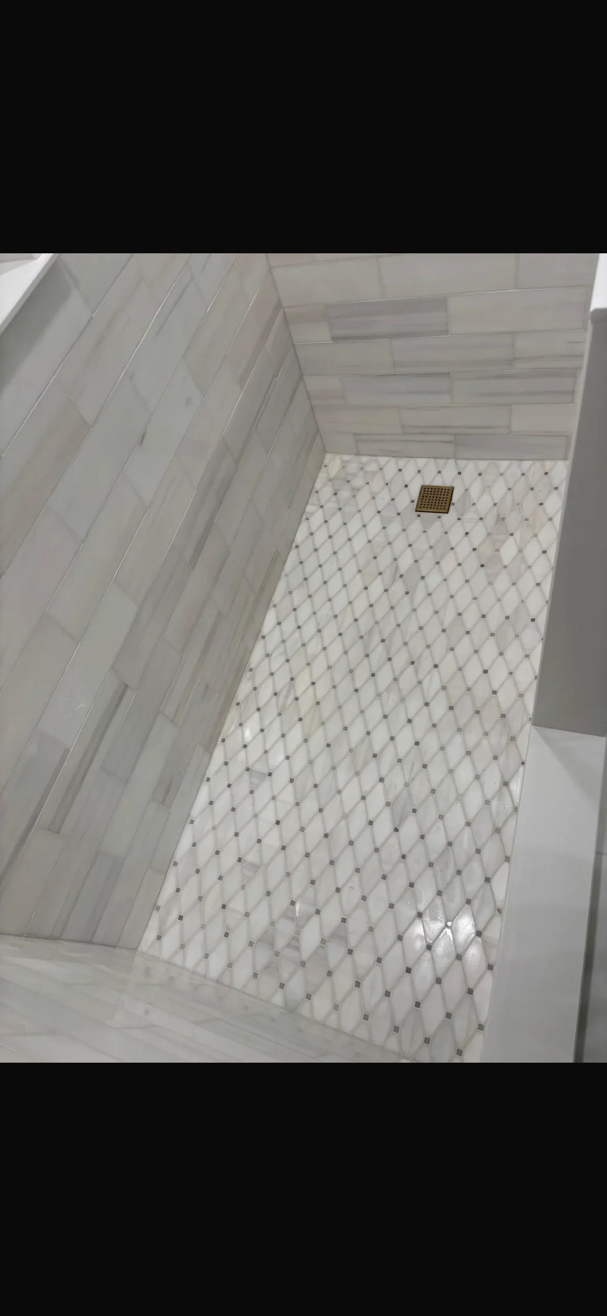 Marble subway tile walls and geometric mosaic floor in completed shower installation