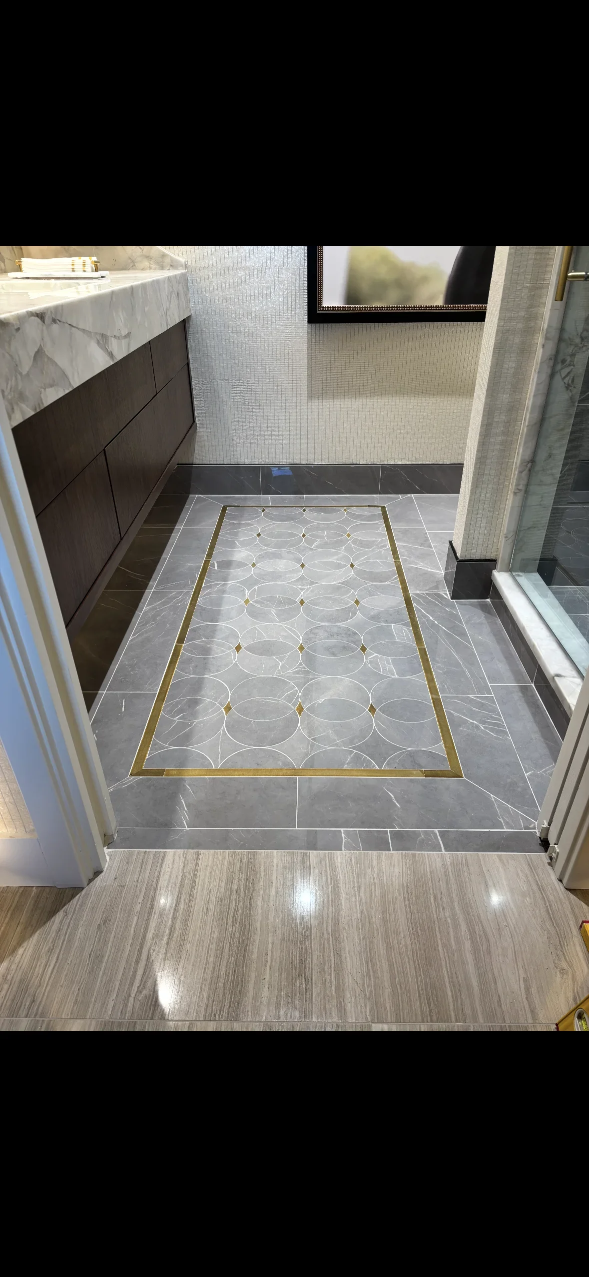Gray marble floor tiles with circular mosaic pattern and brass border in modern bathroom