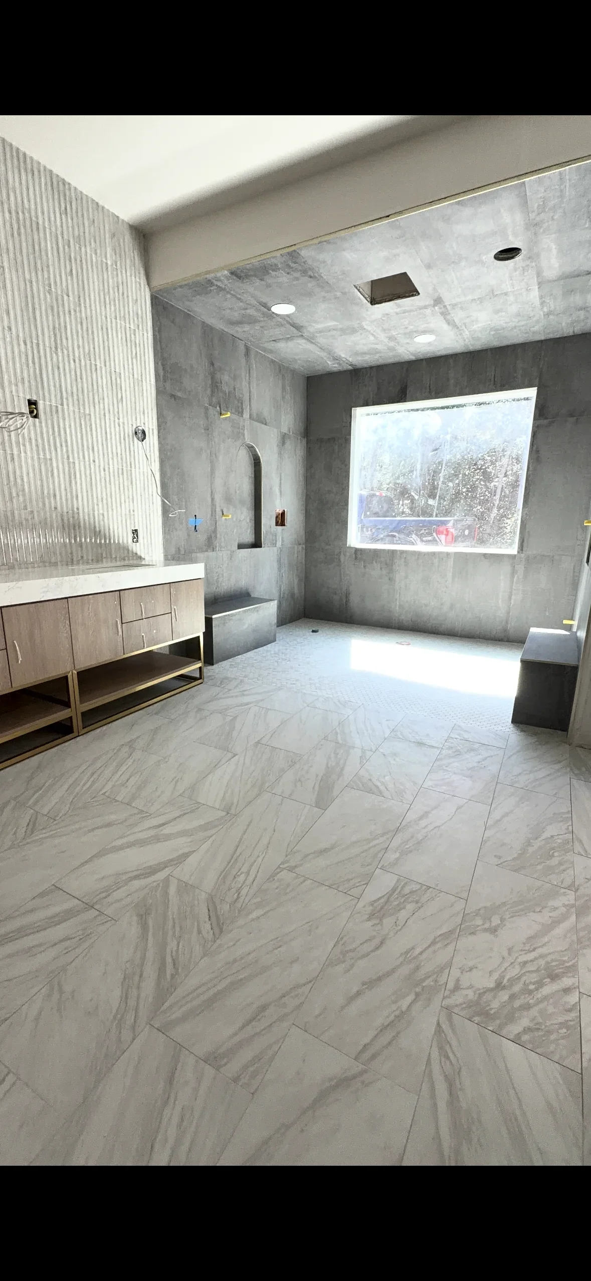 Marble herringbone floor tile and large-format shower wall tile in modern bathroom with concrete ceiling