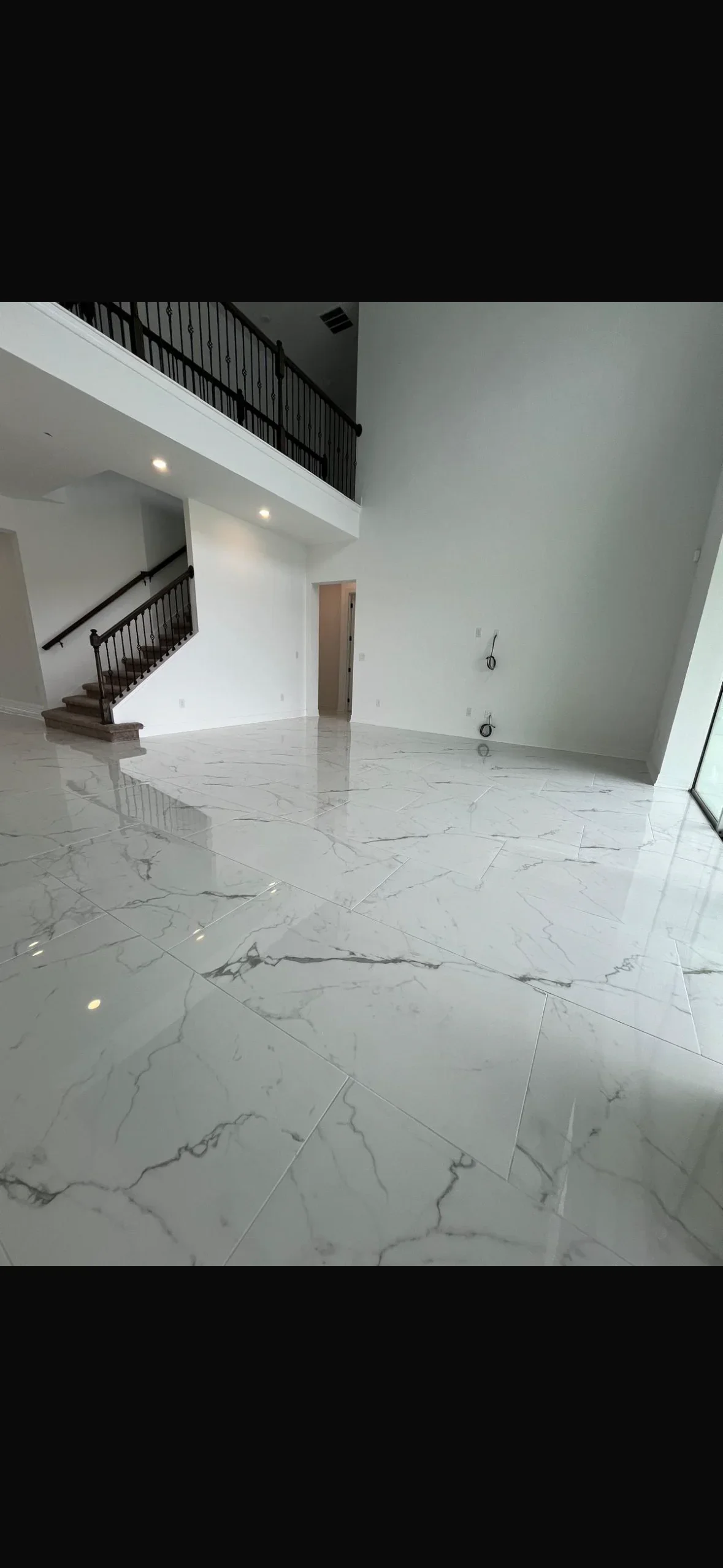 Large format white marble-look porcelain tiles installed in open living area with two-story ceiling