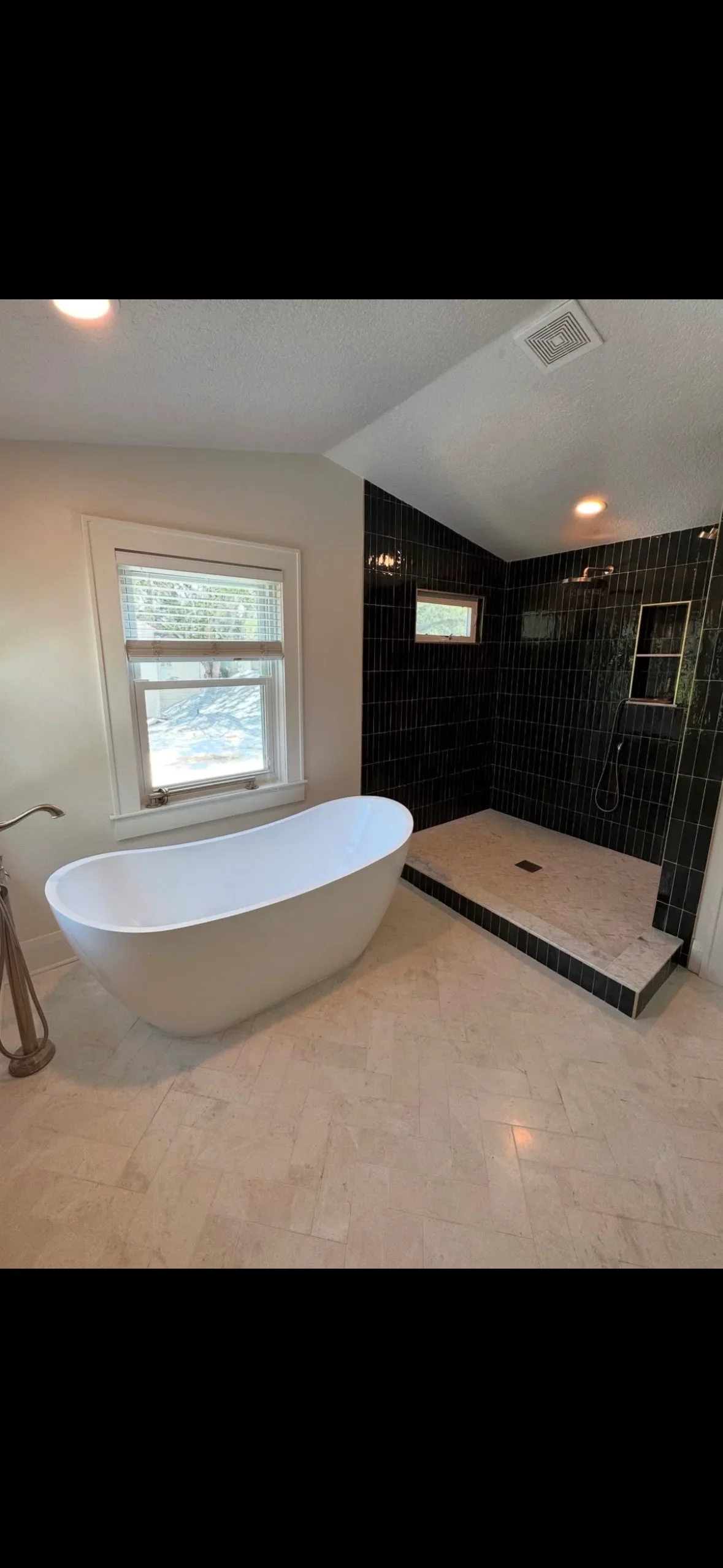 Black subway tile shower with marble base, white soaking tub, travertine floor, and recessed shelving