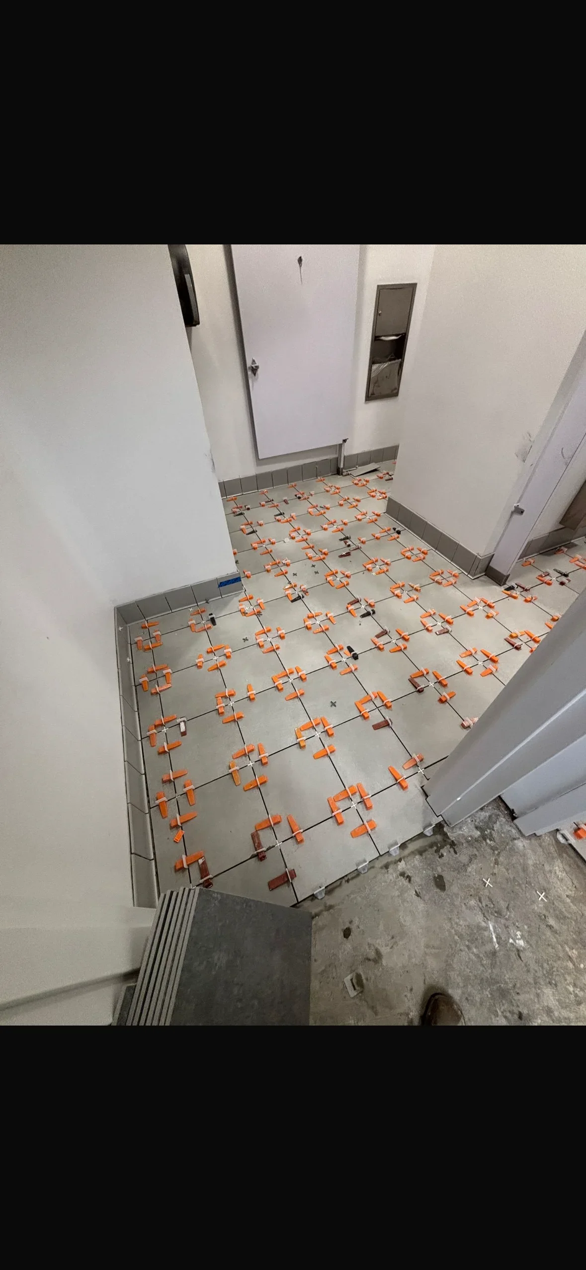 Ceramic tile floor with orange leveling clips installed in commercial bathroom space