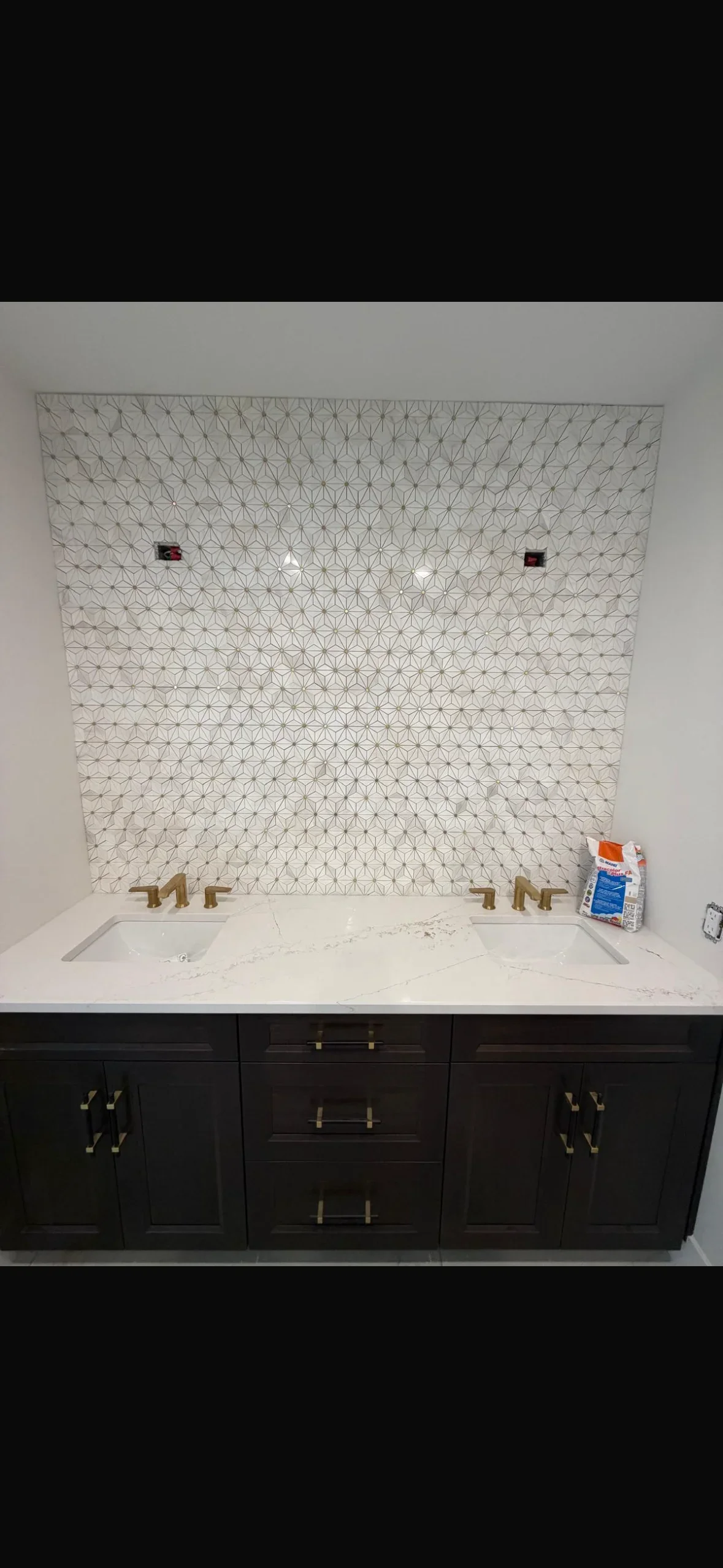 Geometric star pattern mosaic tile backsplash above marble vanity with brass fixtures