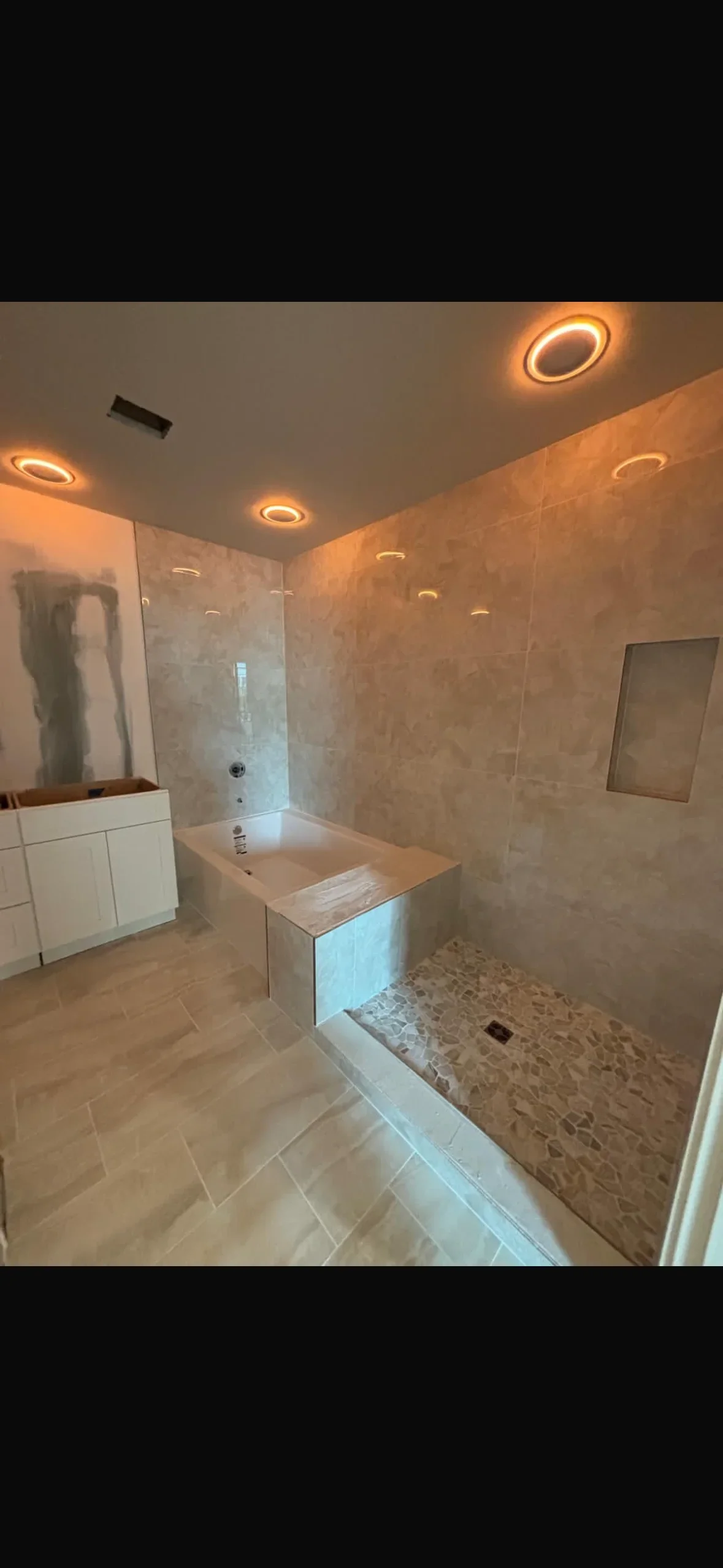 Bathroom with large-format porcelain tile walls, tiled shower enclosure with river rock, and recessed lighting