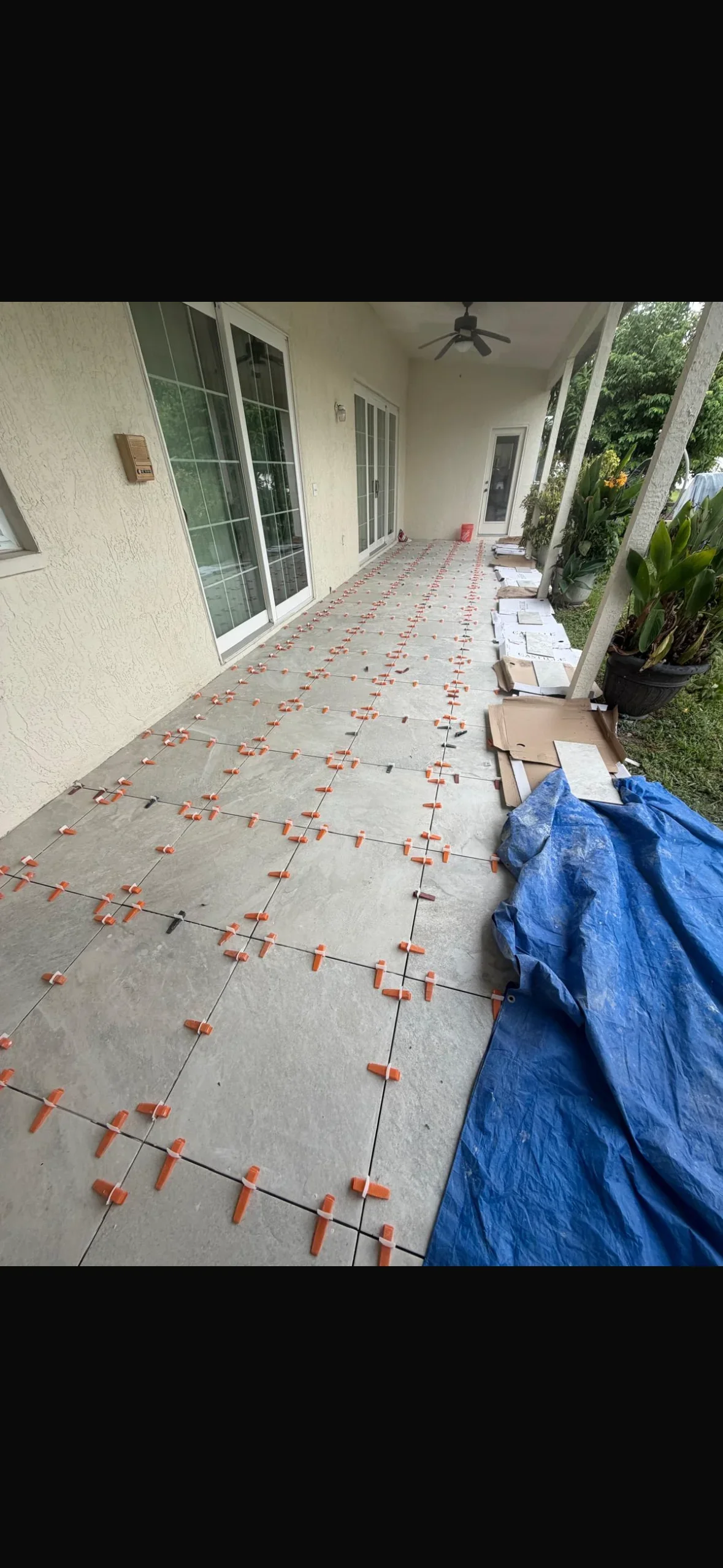 Concrete patio tiles with orange spacers and black grout lines during installation on covered porch