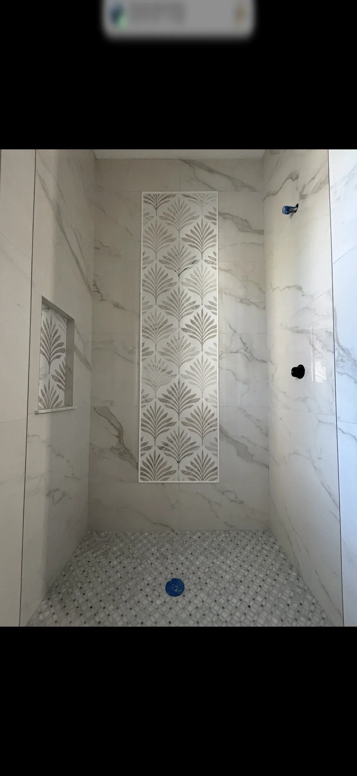 Marble shower with geometric patterned accent tile and hexagonal mosaic floor