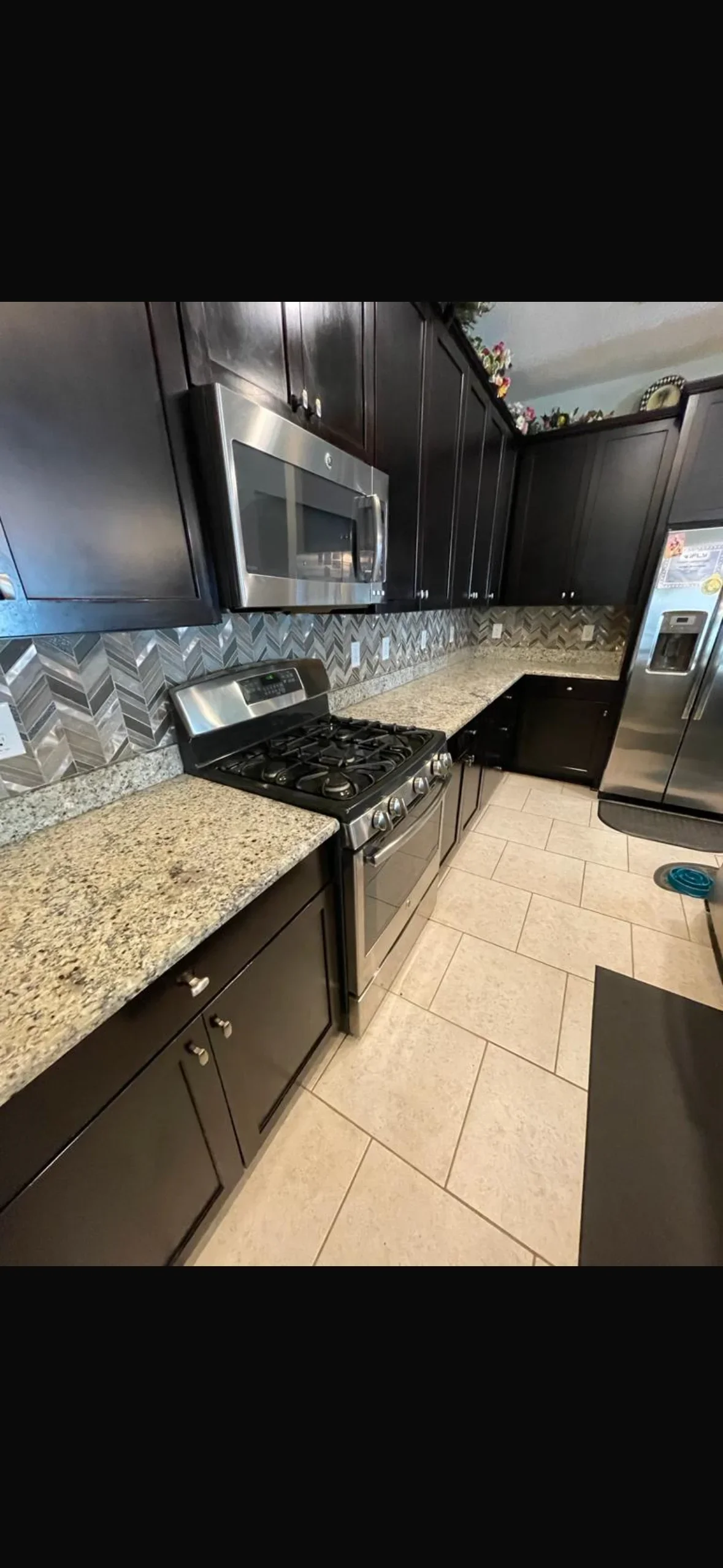 Herringbone marble backsplash and ceramic floor tile in modern kitchen with black cabinets