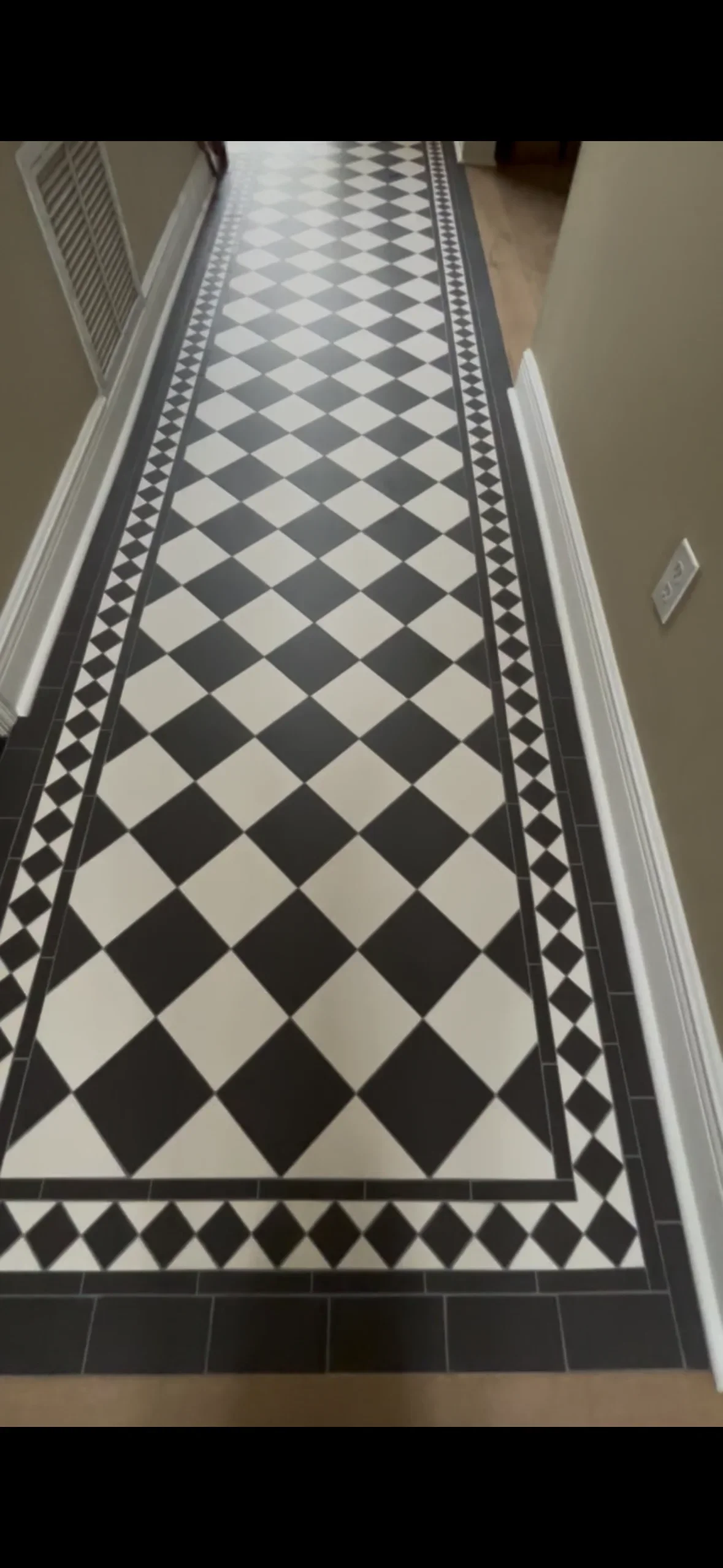 Black and white diamond pattern ceramic tile hallway with decorative geometric border