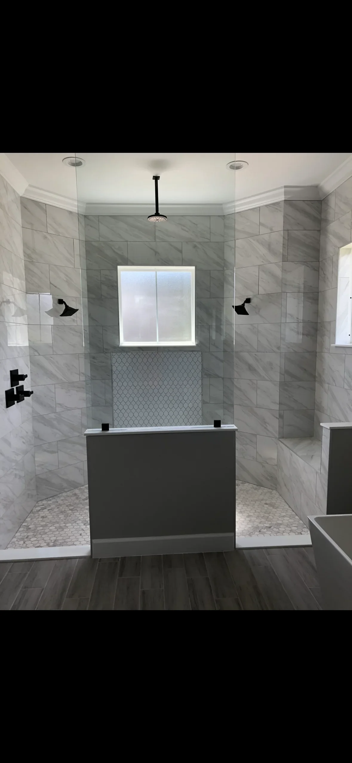 Gray marble tile shower with geometric accent band, pebble floor, and frameless glass enclosure