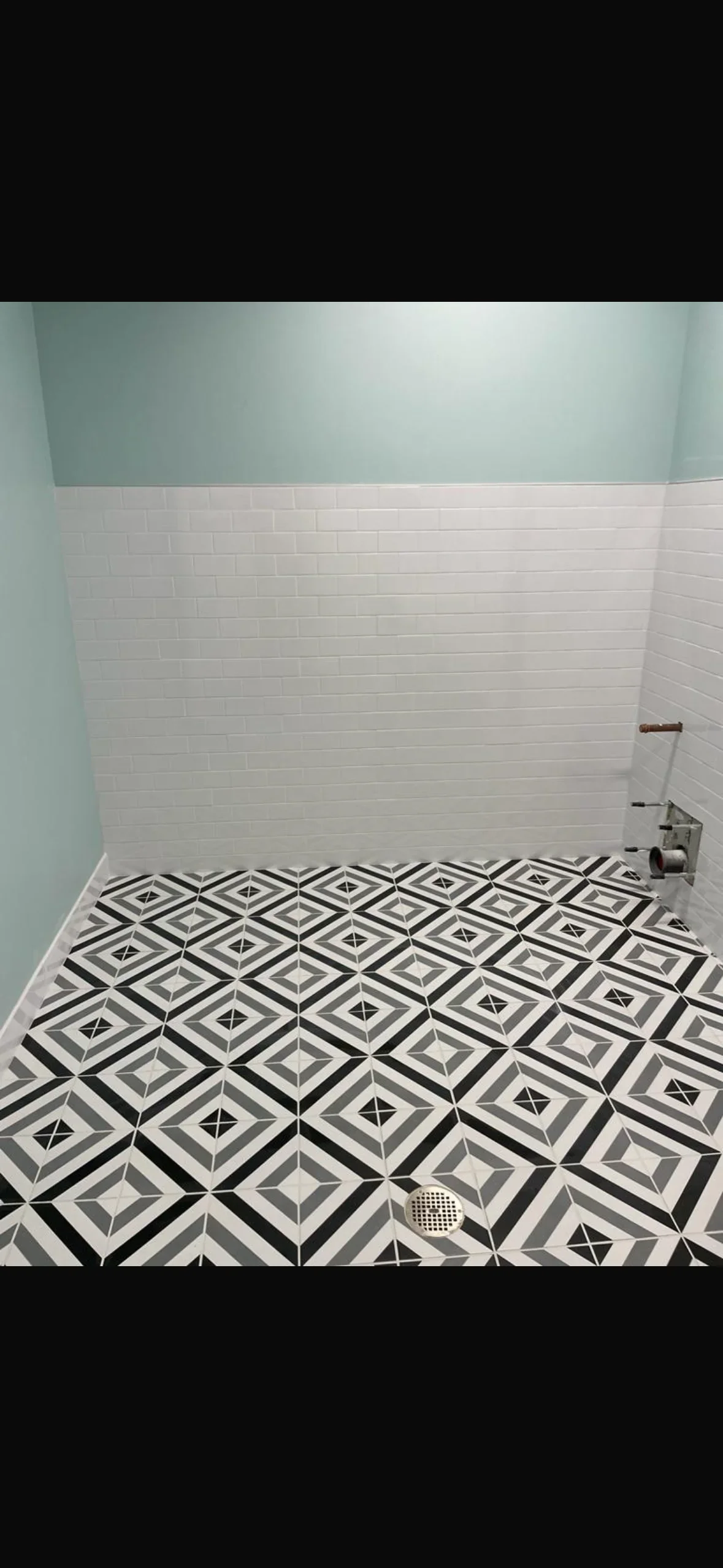 Geometric black and white patterned floor tile with subway tile walls in shower installation