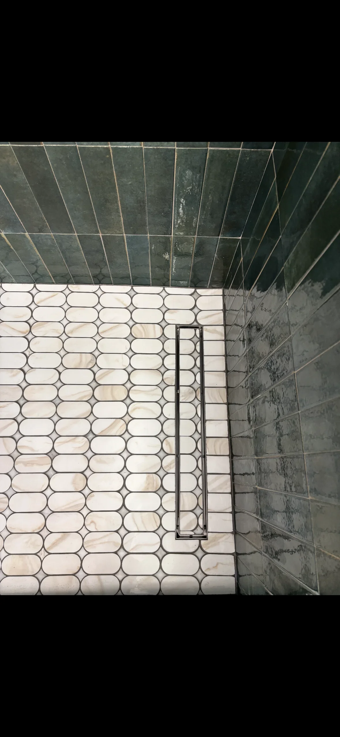 Cream hexagonal mosaic floor tiles with dark gray subway wall tiles and linear drain in shower