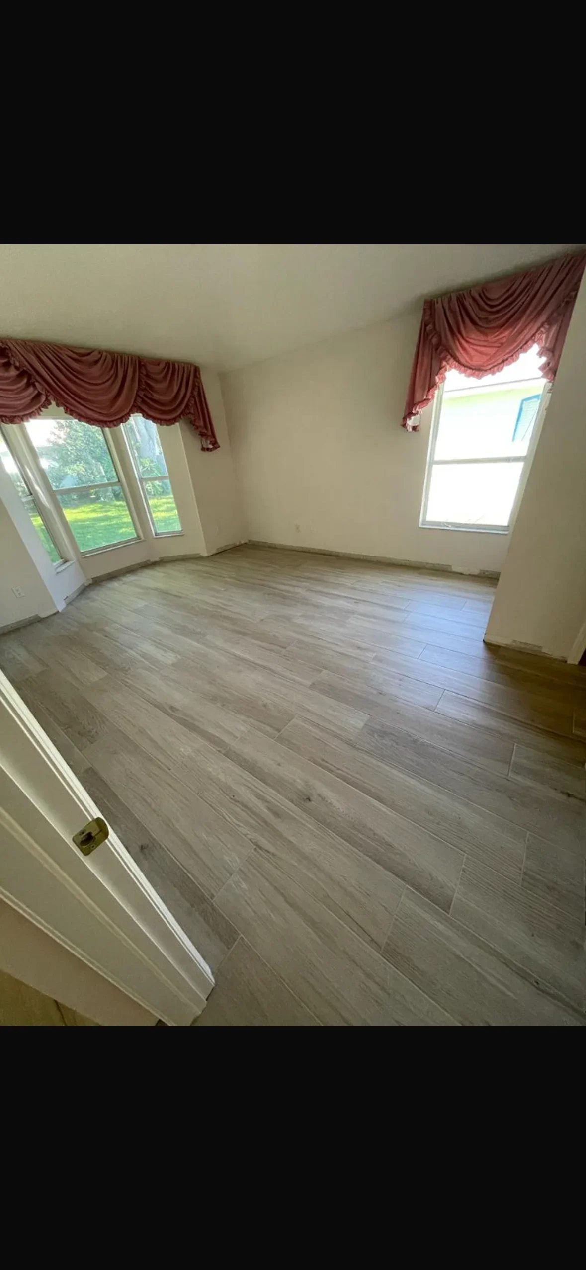 Gray luxury vinyl plank flooring installed in bright room with windows and white trim